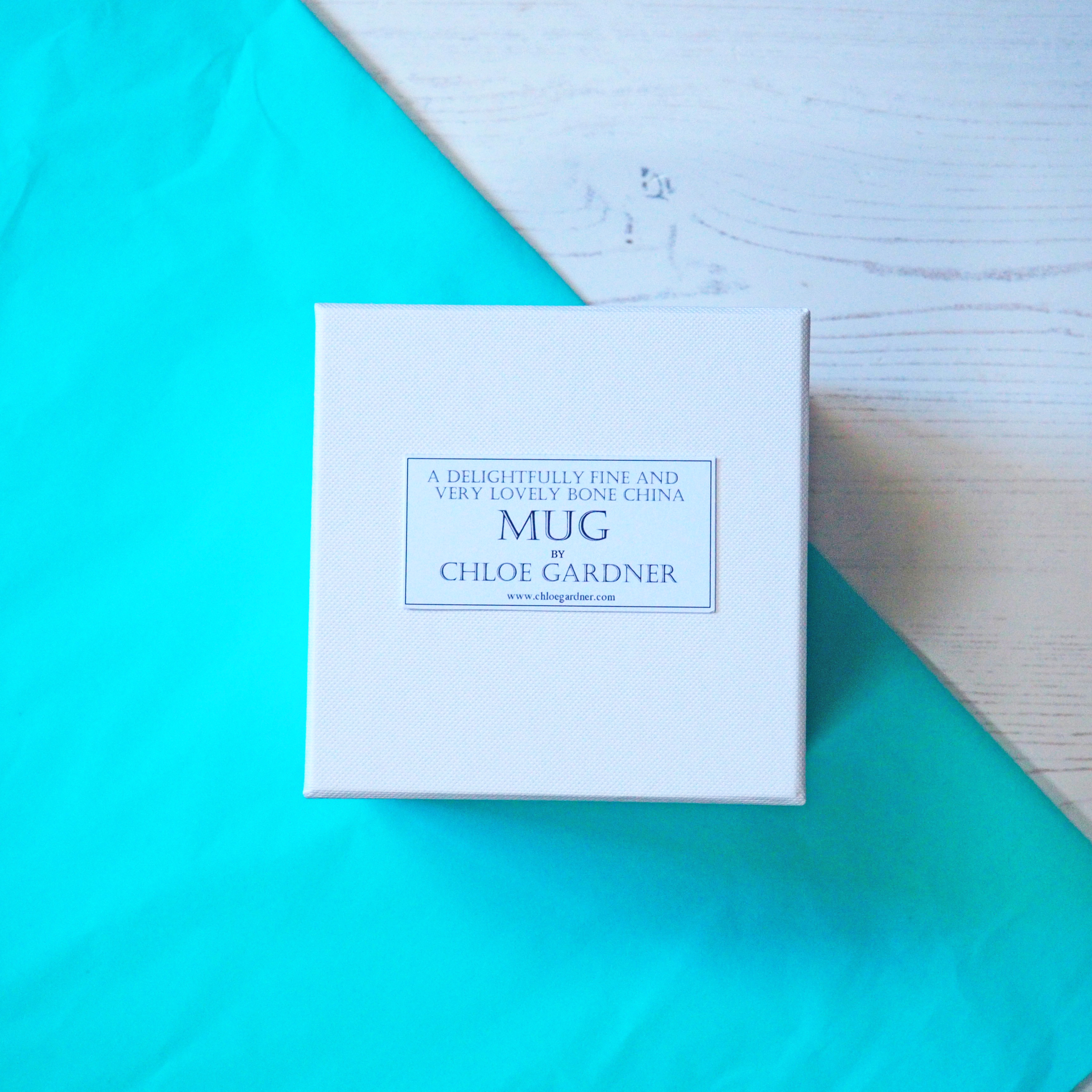 White Luxury Mug Box by Chloe Gardner White Luxury card box square in shape supplied as an option with Chloe Gardner China Mugs. Shown on a white and turquoise background