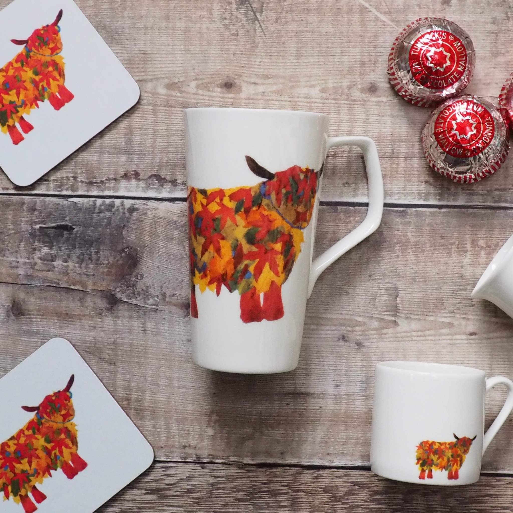 Leaf Highland Cow Latte Mug surounded with leaf Cow Coaster and Leaf COw Espresso mug with teacakes on the side