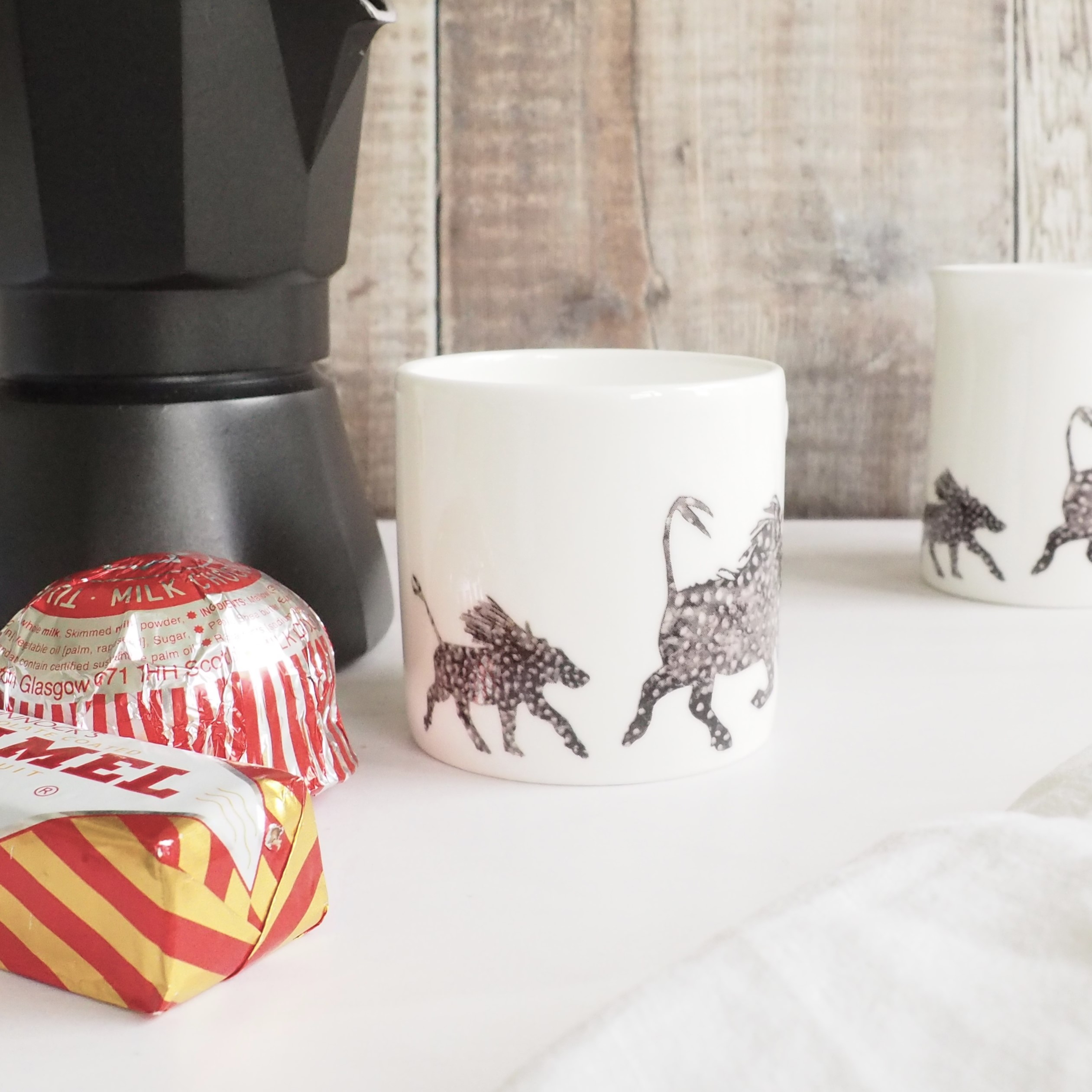 Warthog Espresso mug with row of warthogs Black and white Warthog Espresso Mug by Chloe Gardner pictured with stovetop pot and Tunnocks teacakes